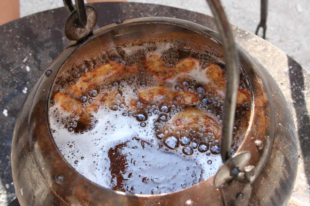 Topf mit Fett, darin krumme Krapfen nach mittelalterlichem Rezept ausgebacken - Kochen im Mittelalter auf der Cadolzburg.